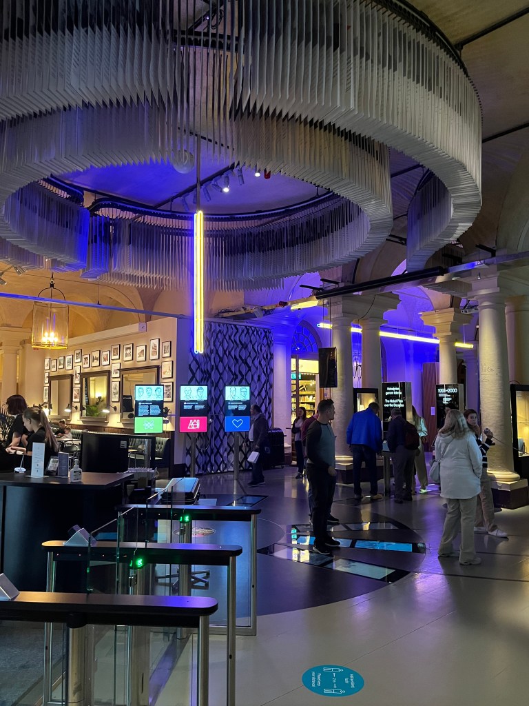 Blick auf den Innenbereich des Nobel-Museums in Stockholm mit modernen Designelementen und Besuchern, die sich um interaktive Ausstellungen versammeln.